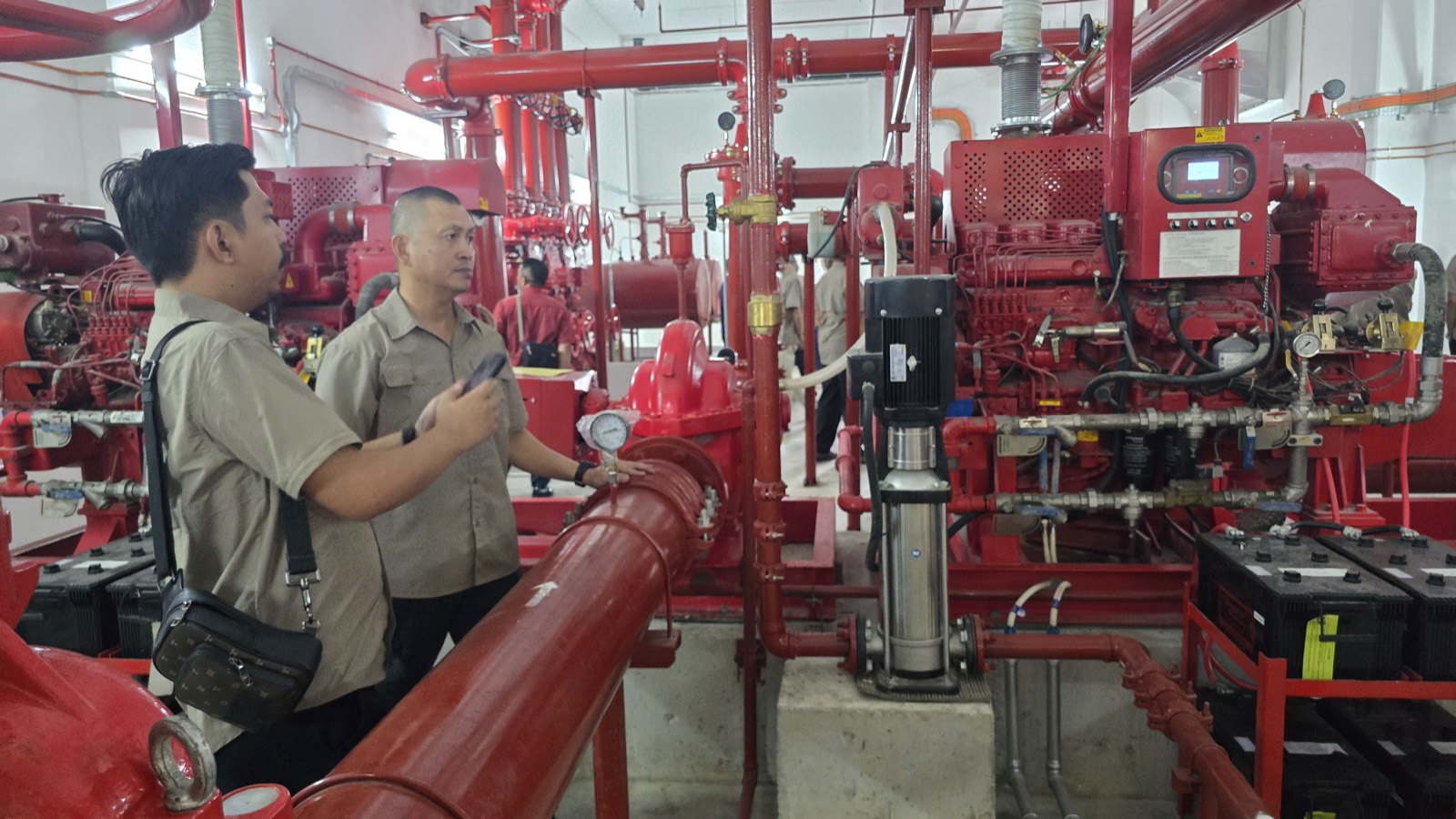 An Otti trainer inspecting a fire pump set and pressure gauge in a building pump room